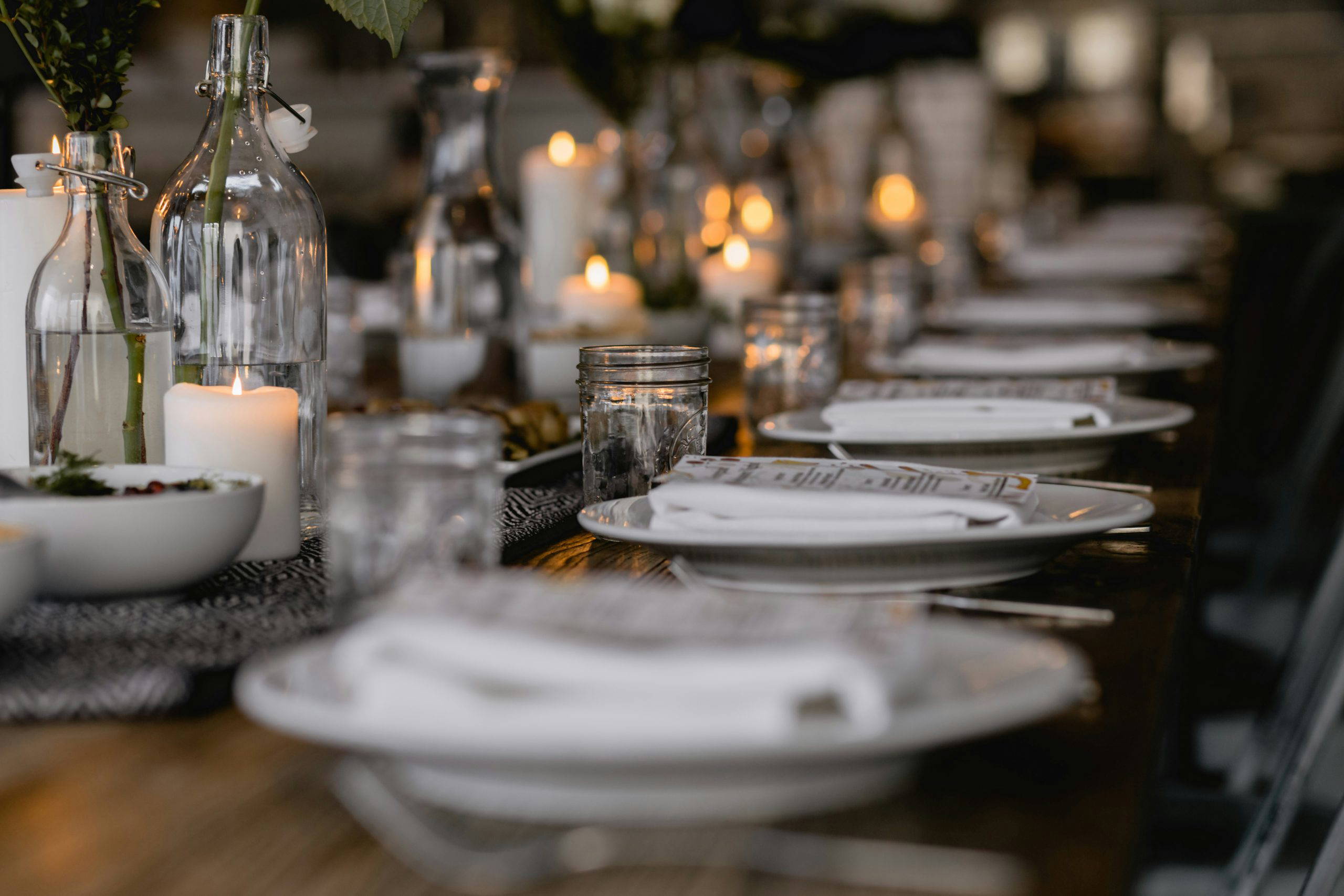 A long dining table elegantly laid with white plates, candles and glass bottles, set and ready for an intimate wake or memorial gathering planned by After.