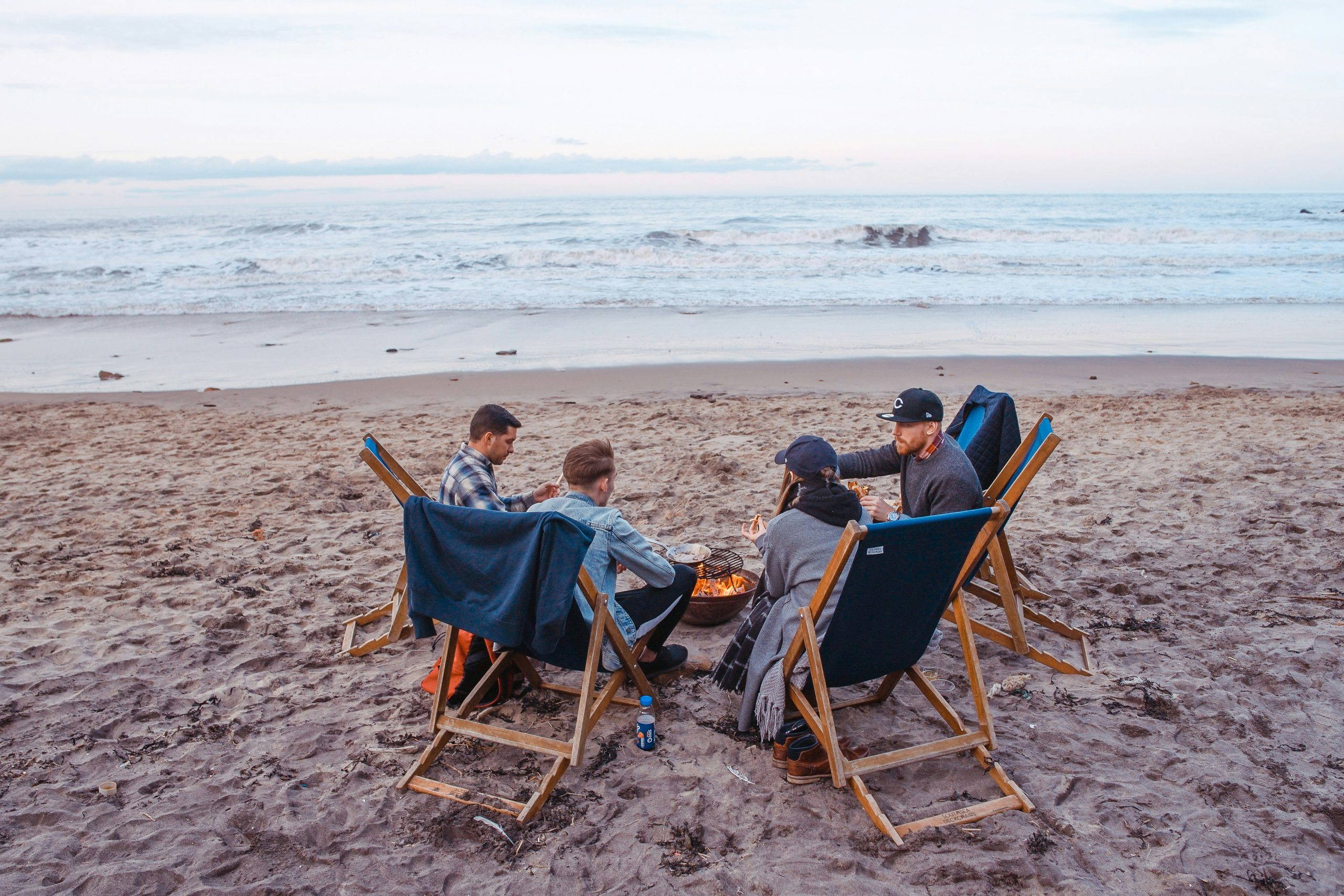 An image of a group of people on a beach around a fire, celebrating a memorial service for their loved one.